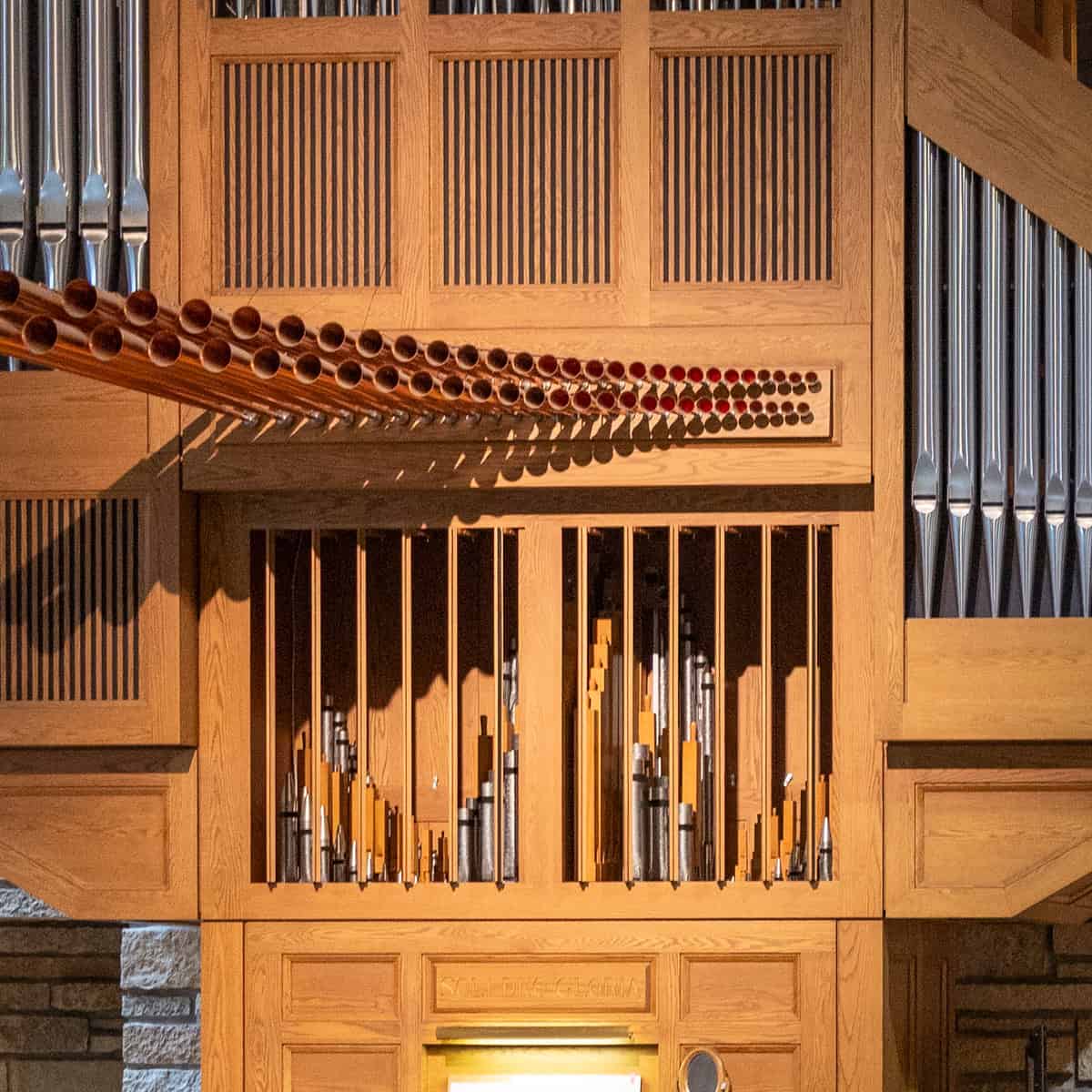Wooden church organ pipes and structure, featuring a detailed arrangement of metallic and wooden elements. Warm lighting highlights intricate craftsmanship and design.