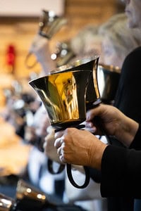 People playing handbells in a group setting, focusing on hands and instruments. The image captures the shiny, metallic handbells mid-performance.