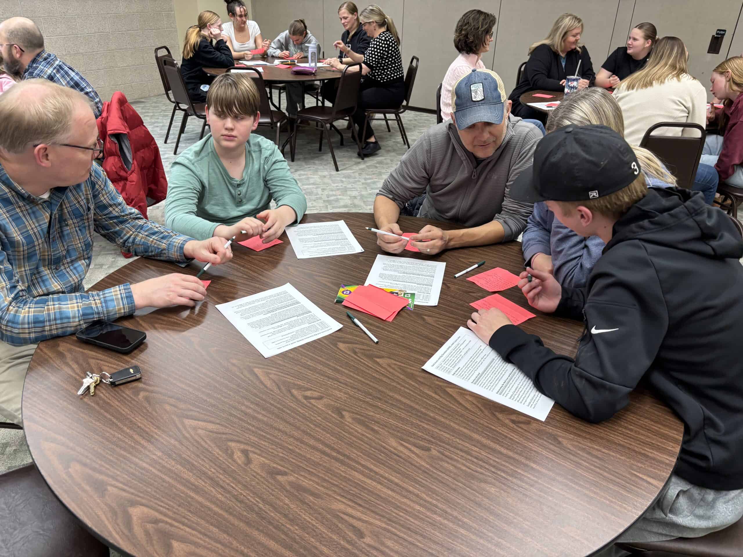 A detailed group discussion at Incarnation Lutheran Church community event, featuring diverse attendees engaging with printed materials around a large round table.