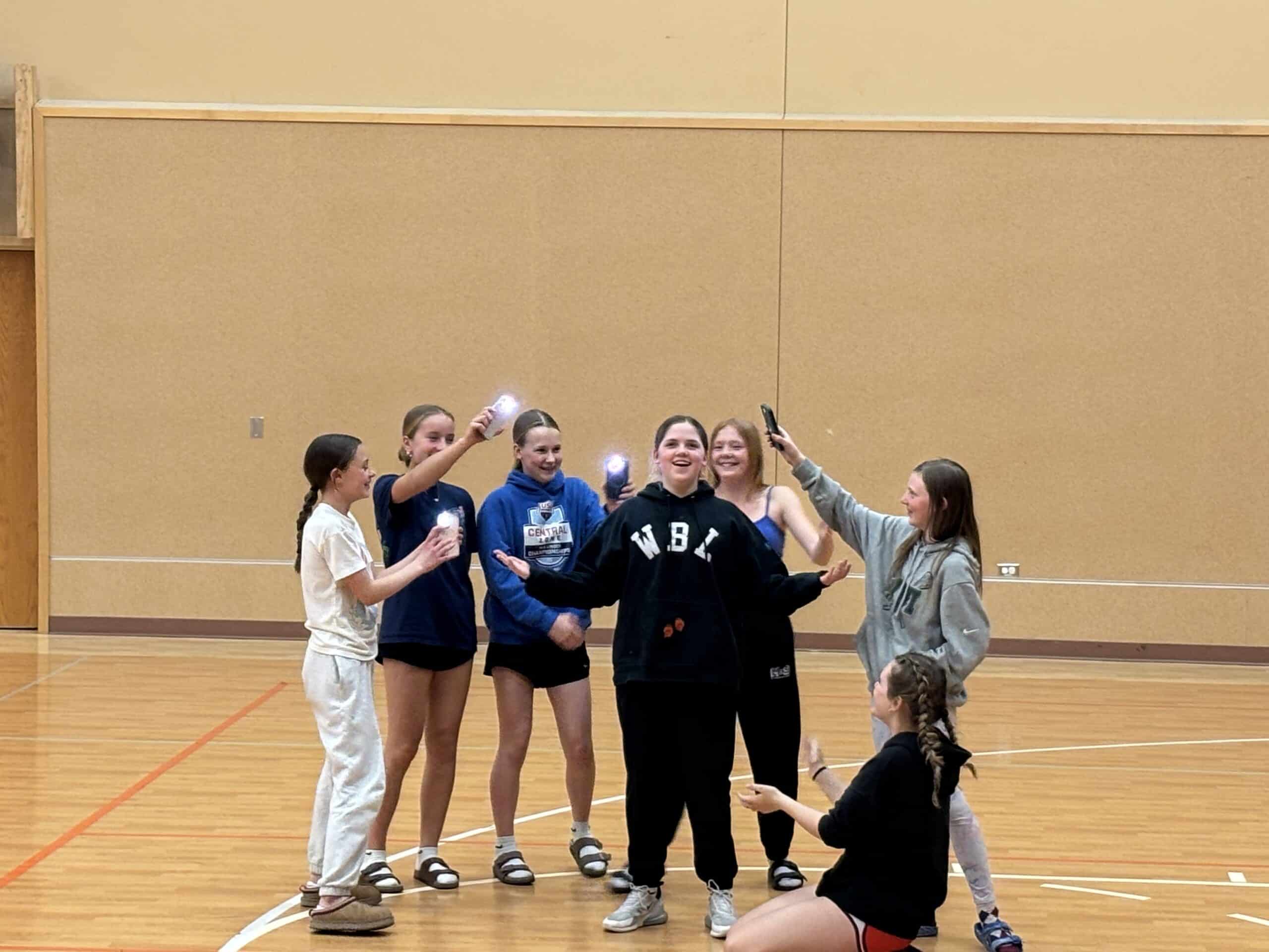 A woman and six girls celebrating with drinks in a gymnasium, likely after a sports event or activity at Incarnation Lutheran Church.