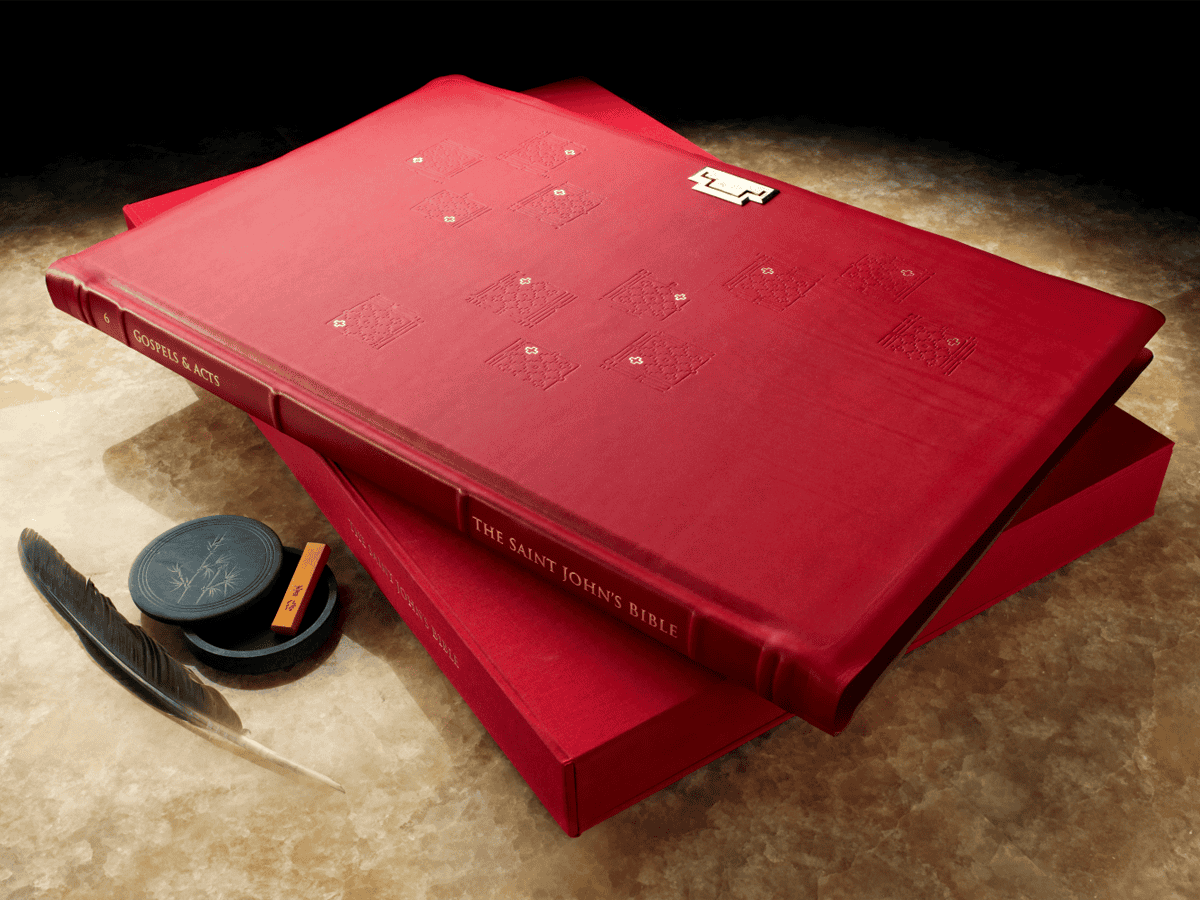 A detailed red Bible with gold embossed lettering resting on a table, accompanied by a quill and inkpot, symbolizing faith and spirituality at Incarnation Lutheran Church.