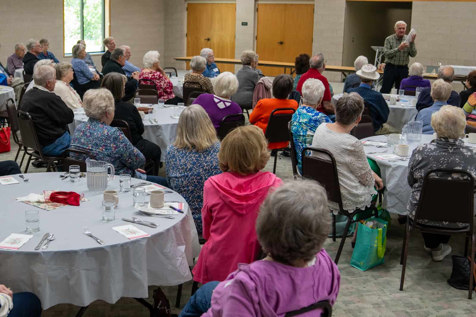 Community gathering at Incarnation Lutheran Church with a speaker addressing a seated audience of diverse seniors and adults.
