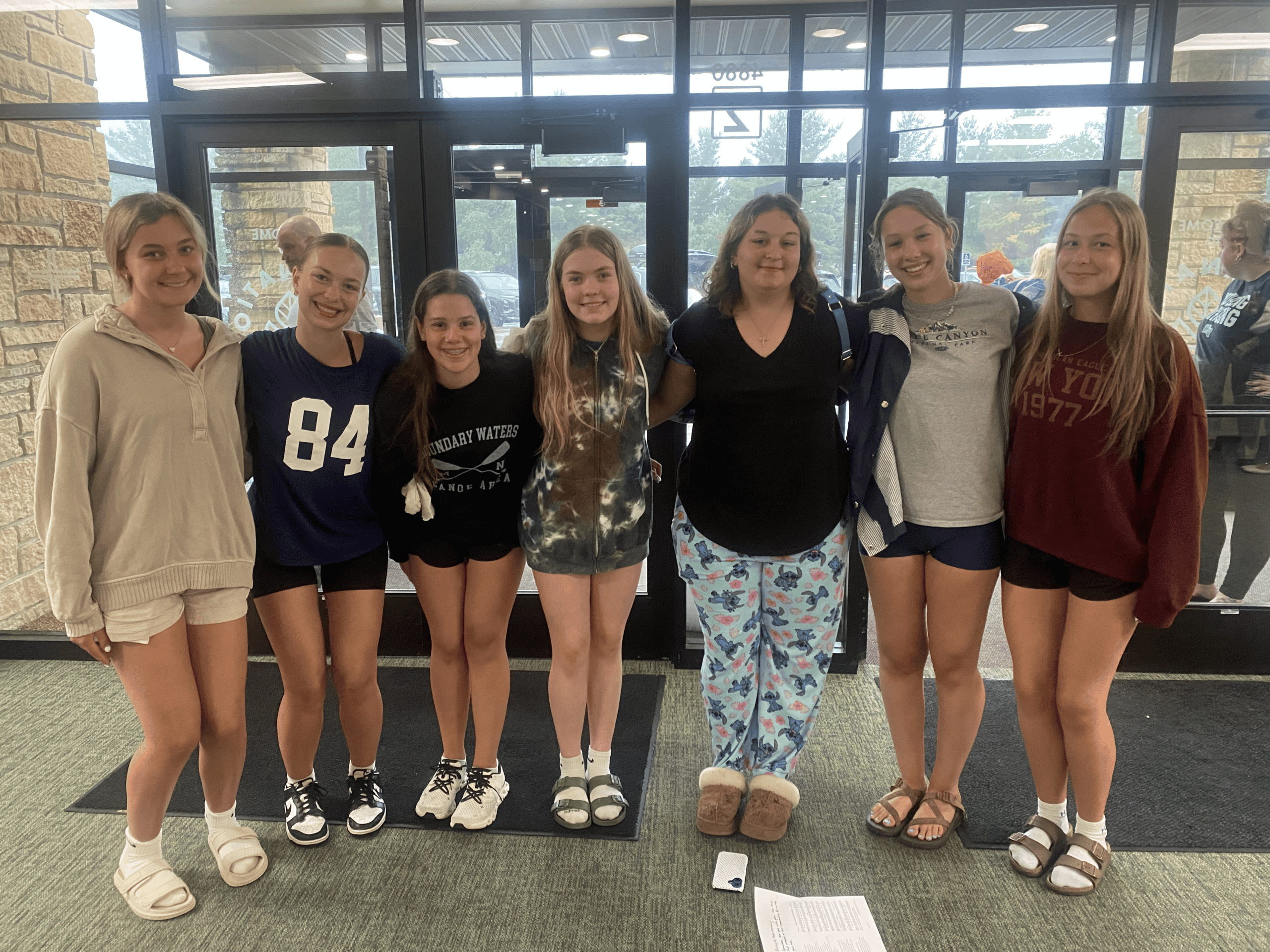 Group of seven girls standing inside Incarnation Lutheran Church, smiling for the photo, with large glass doors behind them.