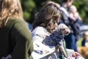 People gathered outdoors at Incarnation Lutheran Church, with a woman holding a small dog in a blue jacket, during a community event.