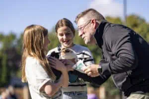 A man and two young girls at Incarnation Lutheran Church holding a small animal during an outdoor event.